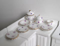 1:12 scale miniature white porcelain dinner set with pink floral pattern and gold rims, set of 12, on a counter