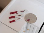 1:12 scale miniature kitchen knives with red handles, set of 3, white blades with a rose print, shown beside a coin