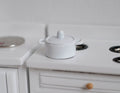 1:12 scale miniature white metal cooking pot with lid and side handles, short size, shown on a white stove