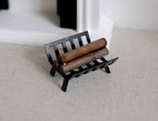 1:12 scale miniature firewood with log rack, black metal rack holding brown logs, shown beside a fireplace
