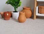 1:12 scale miniature terracotta clay pot with round body and narrow neck, shown beside other pots and a potted plant