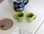 1:12 scale miniature ceramic coffee mugs in green, set of 2, shown beside a coin and a milk pitcher for scale