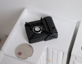 1:10 scale miniature black portable gas stove with a single burner, shown on a white counter beside a coin