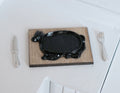 1:12 scale miniature cow shaped black sizzler steak plate with wood board, fork and knife, shown on a white table