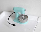 1:12 scale miniature mint green stand mixer with silver bowl and black cord, shown on a white kitchen counter