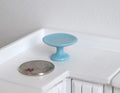 1:12 scale miniature blue ceramic pedestal cake stand, shown on a white kitchen counter beside a coin for scale