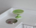 1:12 scale miniature ceramic pedestal cake stand in green, shown beside a coin on a white kitchen counter