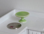 1:12 scale miniature ceramic pedestal cake stand in green, shown beside a coin on a white kitchen counter