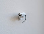 1:12 scale miniature bullet security camera in white with antenna and black cable, shown mounted on a white wall