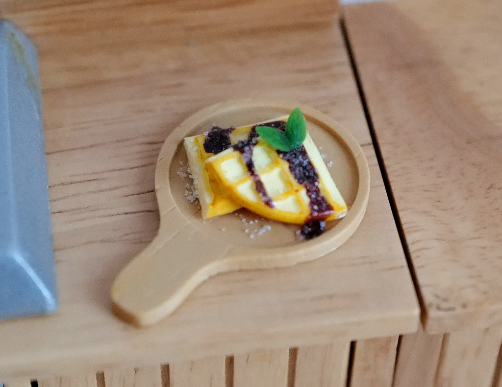 1:12 scale miniature chocolate waffle with banana slices and blueberries on a round wood serving board with handle