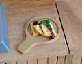 1:12 scale miniature chocolate waffle with banana slices and blueberries on a round wood serving board with handle