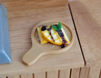 1:12 scale miniature chocolate waffle with banana slices and blueberries on a round wood serving board with handle