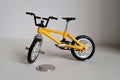 1:12 scale miniature kid size freestyle bike in yellow with front and rear pegs and black tires, beside a coin