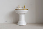 1:12 scale miniature wood pedestal sink in white with a gold rim and gold faucet taps, round basin on a fluted base