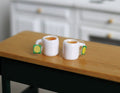 1:12 scale miniature mugs of tea with tea bags, set of 2, white mugs with green and yellow tags, on a wood table