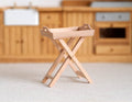 1:12 scale miniature unpainted wood butler tray stand with folding X legs, shown in front of kitchen cabinets