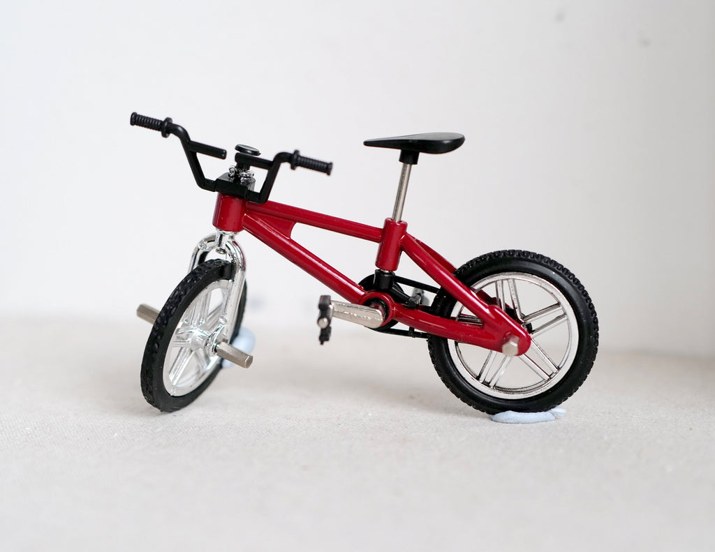 1:12 scale miniature kid's BMX bicycle in red with black tires and silver rims, shown on a white surface