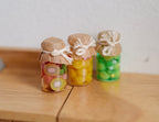 1:12 scale miniature fruit jam jars with tied brown lid covers, set of 3 in red, yellow and green, on a wood table