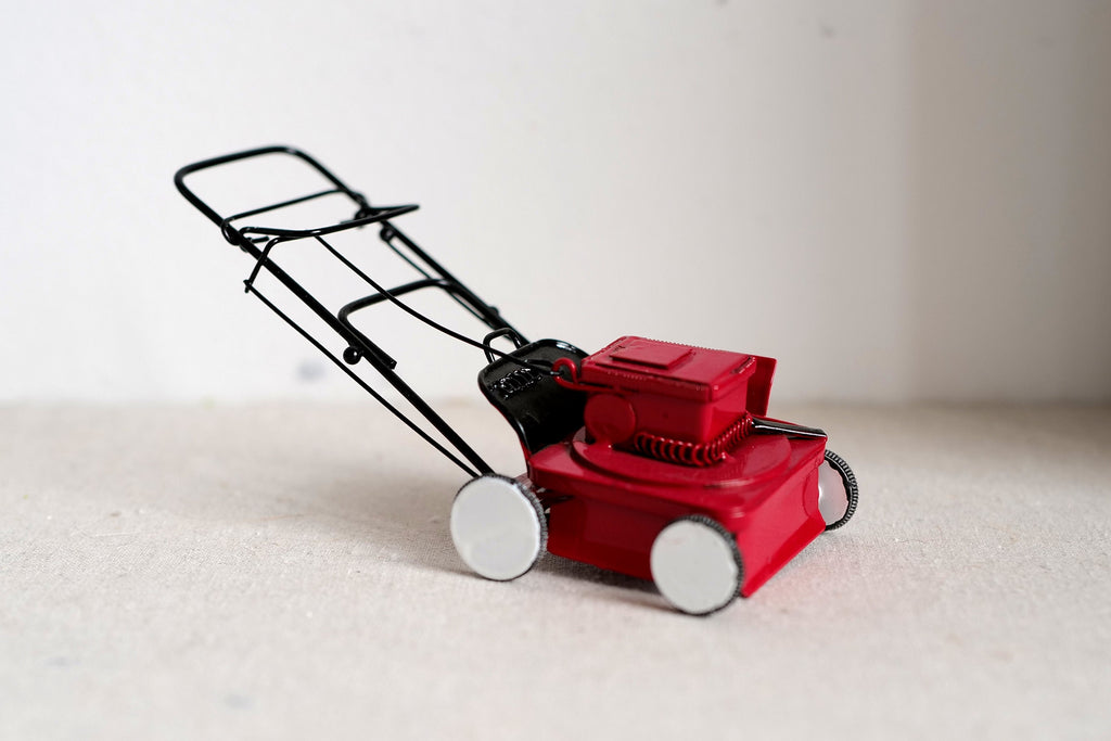 1:12 scale miniature push lawn mower in red with black folding handle and silver wheels, on a light surface