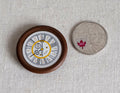 1:12 scale miniature round wall clock in dark brown with Roman numerals and white face, shown beside a coin for scale