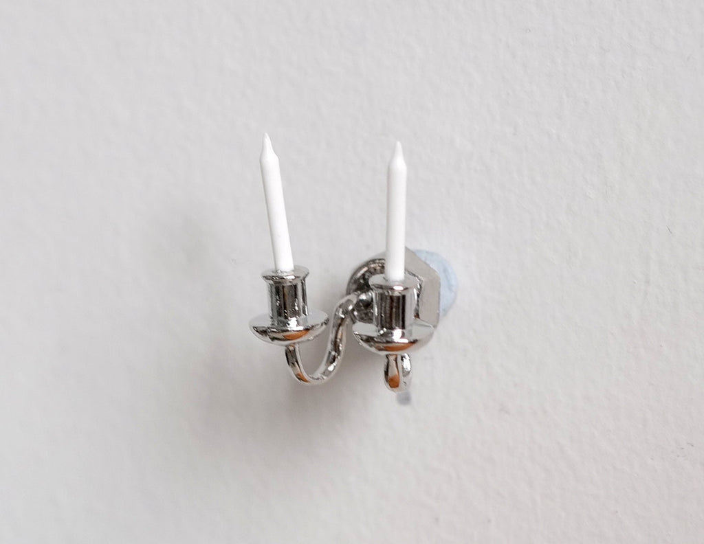 1:12 scale miniature silver wall sconce with 2 arms and white candles, non-electric, shown mounted on a white wall