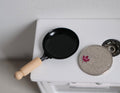 1:12 scale miniature frying pan in black with wood handle, shown on a white stovetop beside a coin for scale