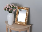 1:12 scale miniature ornate rectangular mirror with gold frame, shown on a wood side table beside a vase of roses