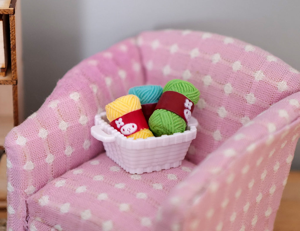 1:12 scale miniature white square knitting basket with 4 colorful yarn skeins, shown on a pink polka dot armchair