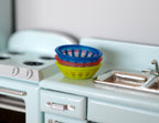1:12 scale miniature square baskets in blue, red and yellow green, set of 3, stacked on a light blue kitchen counter