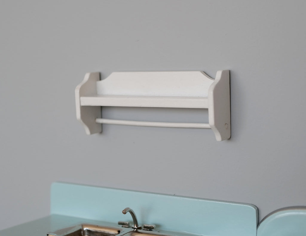 1:12 scale miniature wood plate rail wall shelf in white with shaped side brackets, mounted on a gray wall