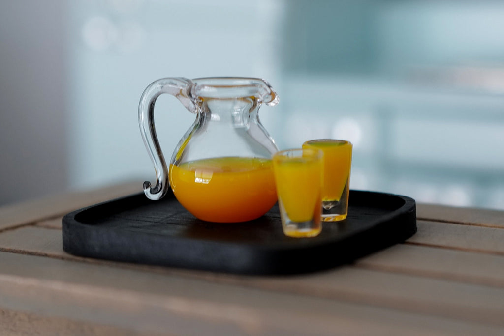1:12 scale miniature orange juice set with clear jug, 2 glasses and black tray, set of 4, shown on a wood table