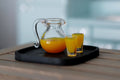 1:12 scale miniature orange juice set with clear jug, 2 glasses and black tray, set of 4, shown on a wood table