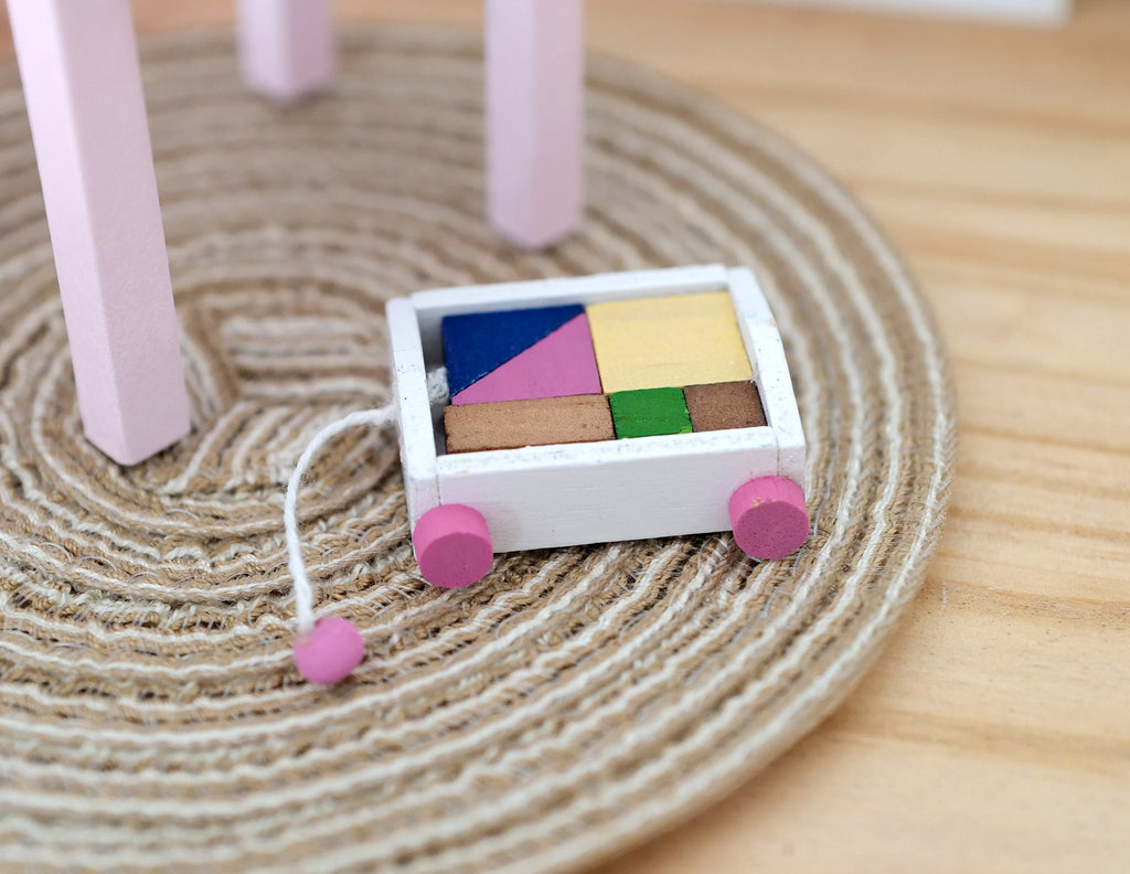 1:12 scale miniature wood pull along wagon with colorful building blocks, pink wheels, shown on a braided rug
