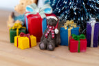 1:12 scale miniature Christmas teddy bear in brown with Santa hat and scarf, extra small, shown among wrapped gifts