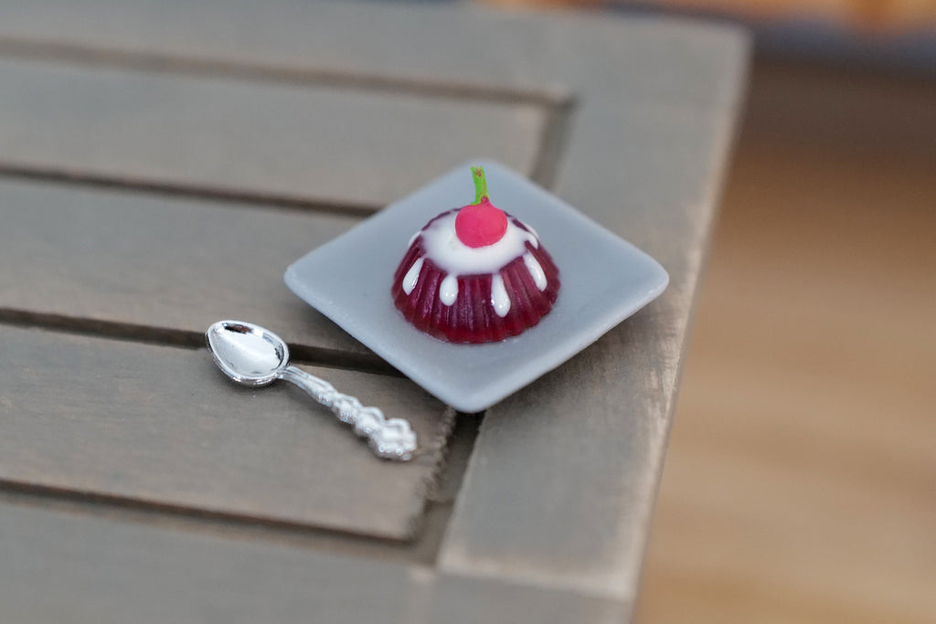 1:12 scale miniature blueberry dome dessert with plate and silver spoon, glossy purple dome, shown on a gray wood table