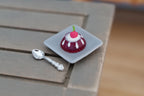 1:12 scale miniature blueberry dome dessert with plate and silver spoon, glossy purple dome, shown on a gray wood table