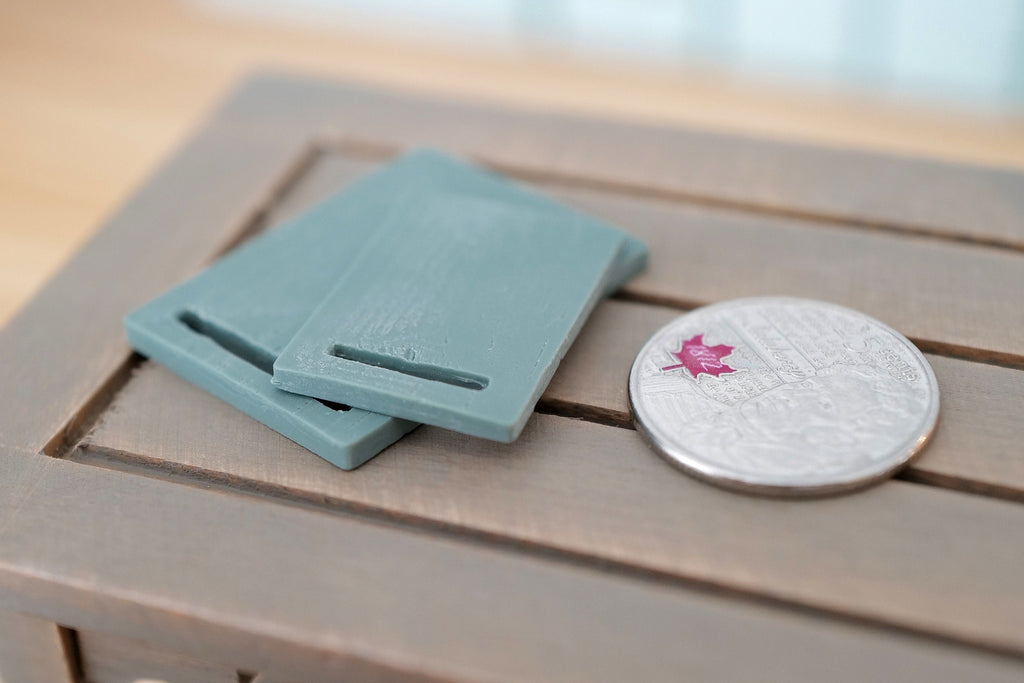 1:12 scale miniature wood cutting boards in sage green with handle slots, set of 2, on a wood table beside a coin