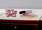 1:12 scale miniature ground meat on a wood cutting board with a cleaver, shown on a dark wood kitchen counter