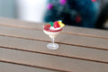 1:12 scale miniature Christmas cocktail with berries, creamy red and white drink in a stemmed glass, on a wood table