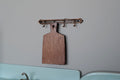 1:12 scale miniature wood cutting board with wall hanger, dark brown paddle board hanging from a metal hook rail