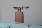 1:12 scale miniature wood cutting board with wall hanger, dark brown paddle board hanging from a metal hook rail