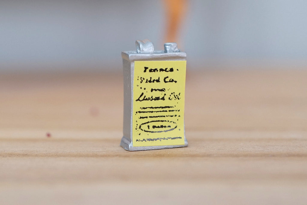 1:12 scale miniature linseed oil metal can with yellow label and silver cap, shown on a wood surface