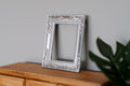 1:12 scale miniature ornate rectangular picture frame in silver, empty frame leaning on a wall above a wood dresser
