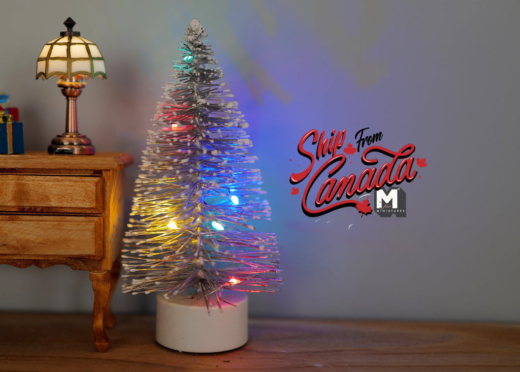 1:12 scale miniature tinsel Christmas tree in silver with multicolor LED lights, white base, shown beside a dresser