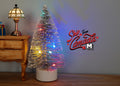 1:12 scale miniature tinsel Christmas tree in silver with multicolor LED lights, white base, shown beside a dresser