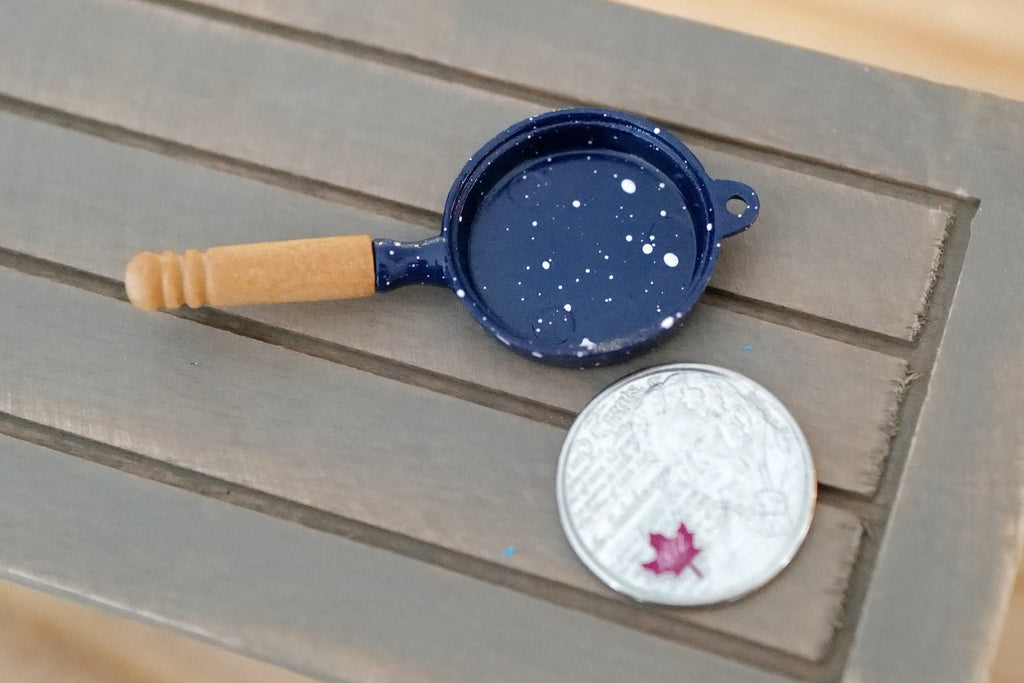1:12 scale miniature navy blue metal frying pan with speckled enamel look and wood handle, shown beside a coin for scale