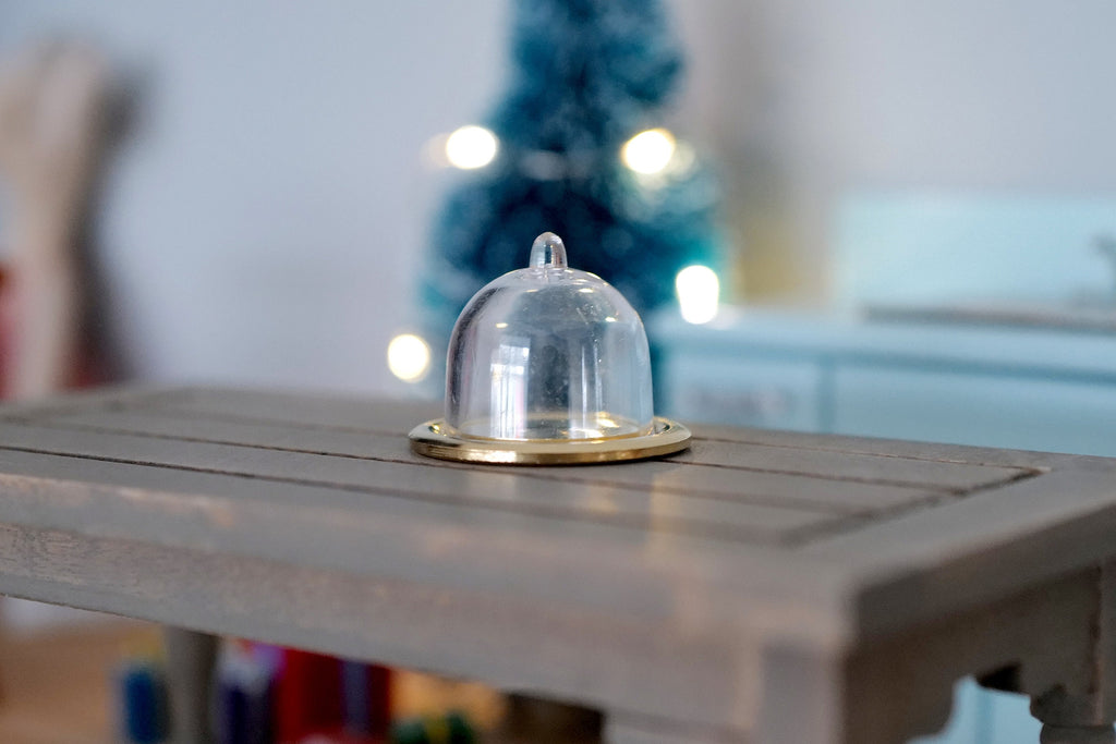 1:12 scale miniature cake dome with round gold metal plate, clear cover, shown on a gray wood table