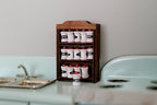 1:12 scale miniature wood spice rack in brown with fixed drawers and 15 white spice jars, on a kitchen counter