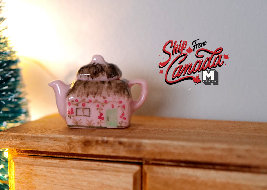 1:12 scale miniature ceramic teapot with lid in pink with floral decoration, shown on a wood dresser