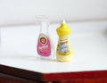 1:12 scale miniature detergent bottles in pink and yellow, set of 2, a clear spray bottle and a dish soap bottle on a counter